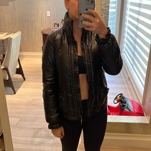 Black shiny puffer jacket with ruffled sleeve and pocket detail.